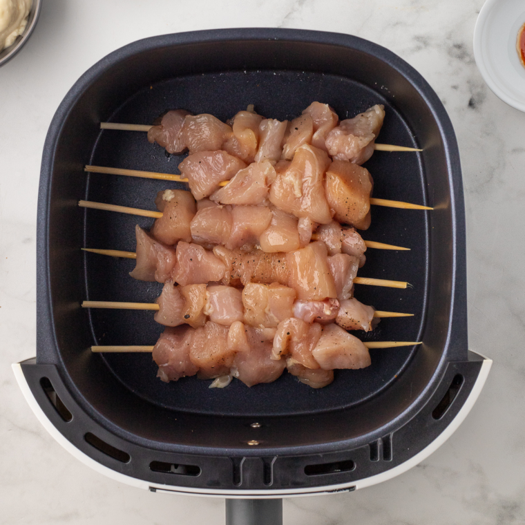 Chicken skewers cooking in air fryer basket brushed with sauce