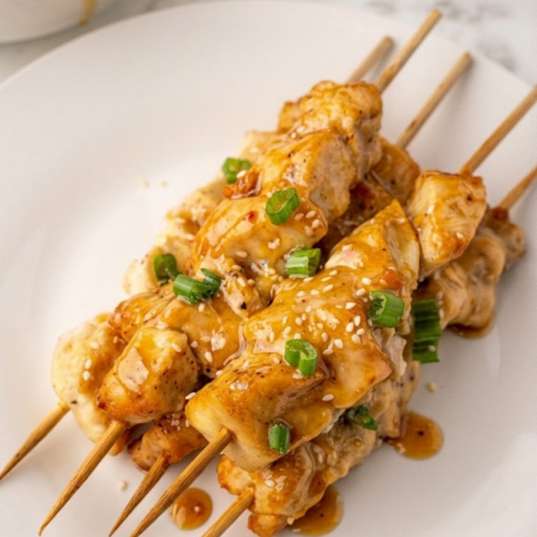 Golden air fryer bang bang chicken skewers coated in creamy spicy sauce served on a plate.