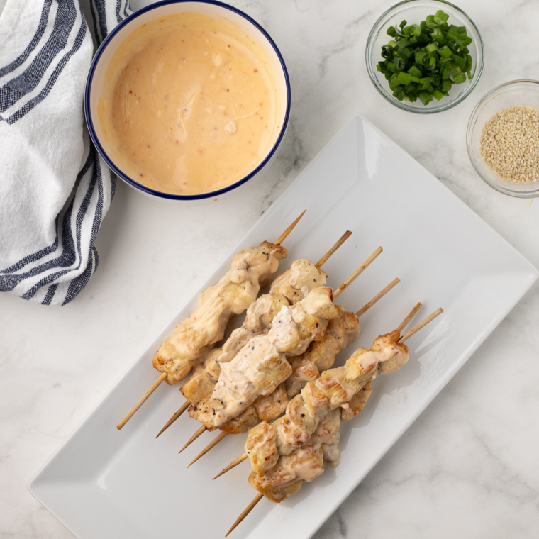 Glazed chicken skewers topped with green onions and sesame seeds served hot