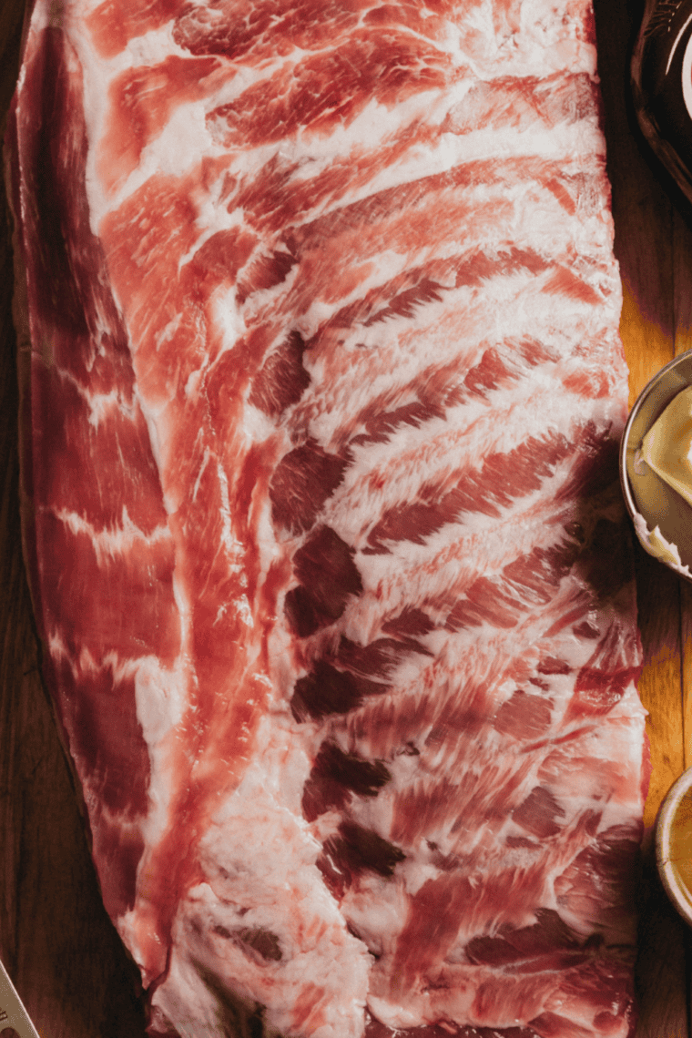 Paring knife peeling silver membrane off the back of a raw beef rib rack.