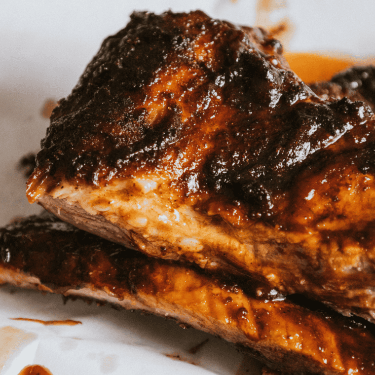 Cooked beef ribs resting under loosely tented foil on a wooden cutting board