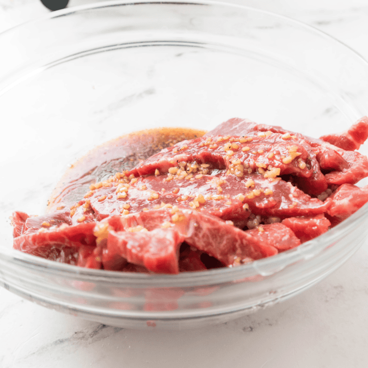 Thinly sliced beef tossed in bulgogi marinade in a bowl to coat before air frying.