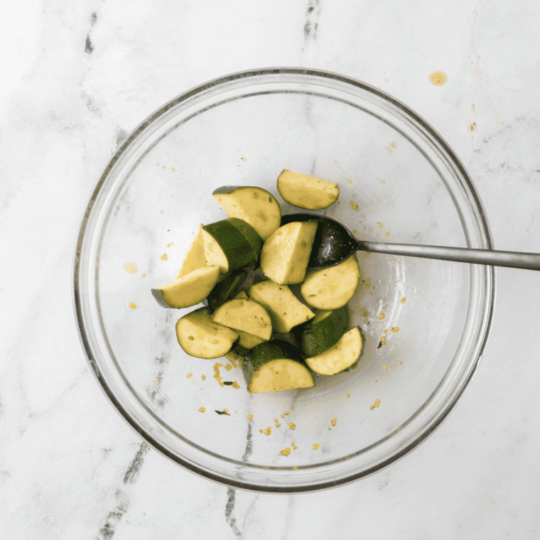 Fresh zucchini half-moons tossed with oil and salt on a plate before air frying.