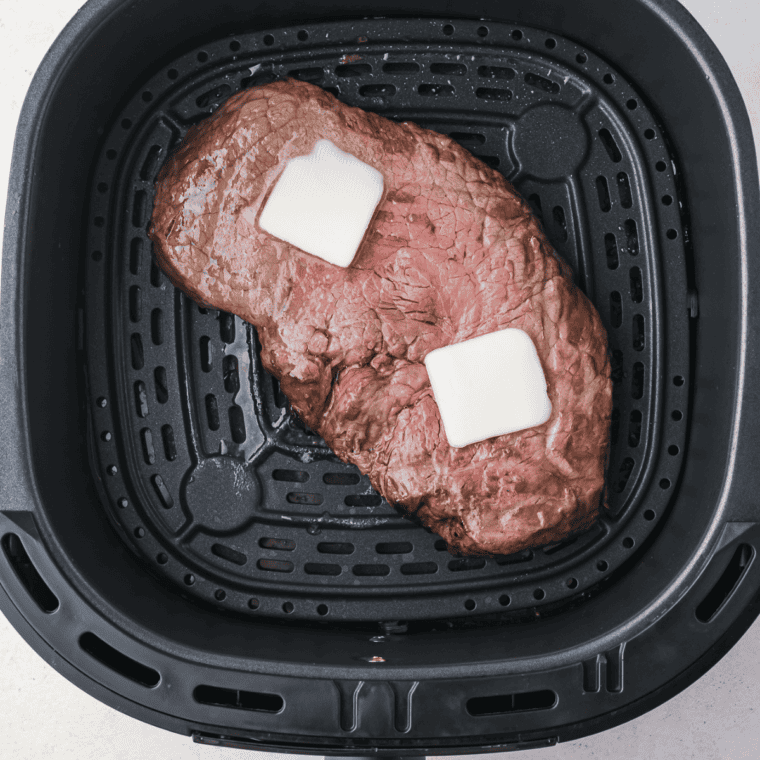 Two seasoned round steaks arranged in a single layer in the air fryer basket