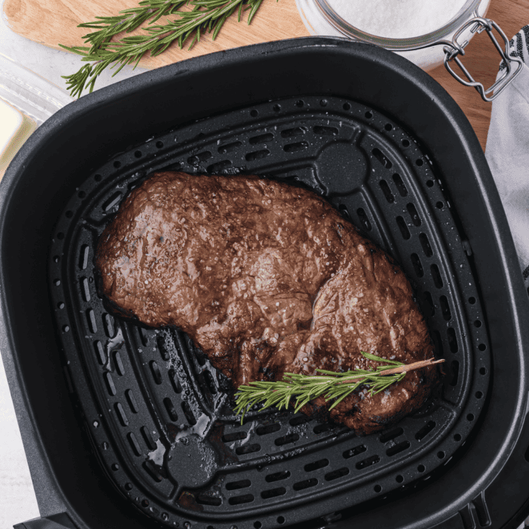 Air fryer round steak being flipped with tongs at the halfway point