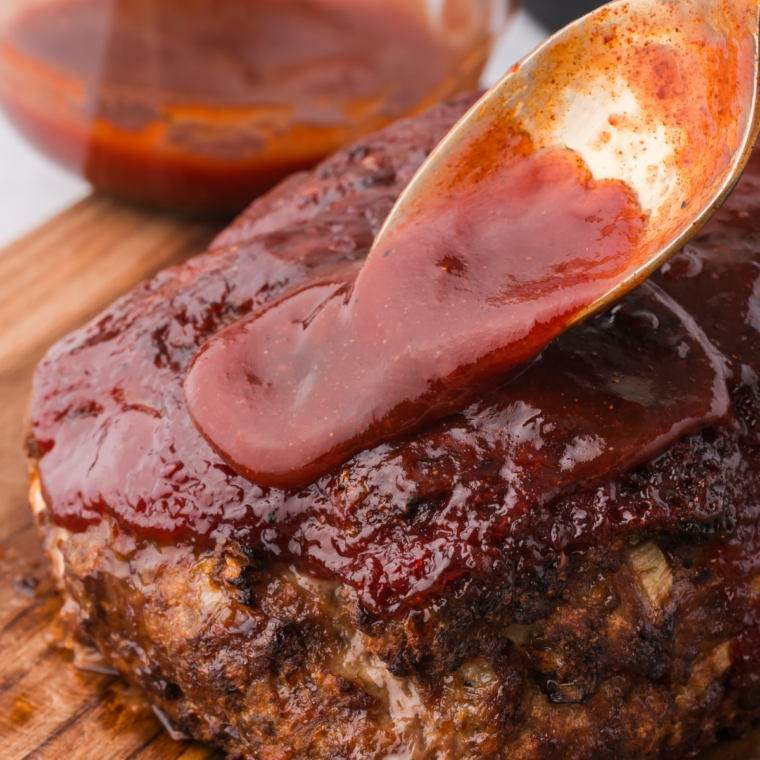 Hands mixing ground beef with seasoning in a glass bowl