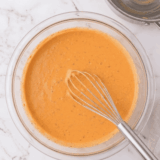 Copycat Burger King Buffalo Sauce in a glass mason jar with a spoon lifting creamy orange sauce