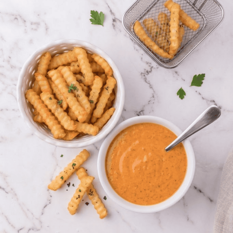 Cup of Burger King buffalo sauce next to crispy chicken nuggets and fries.