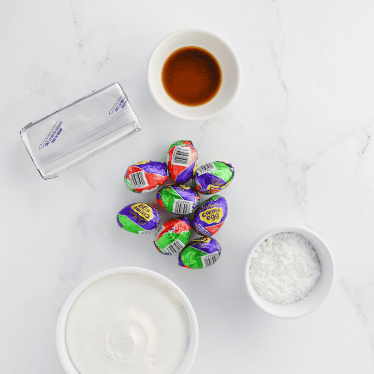All ingredients for Cadbury Egg Dip laid out: cream cheese, powdered sugar, whipped topping, Mini Eggs, and vanilla extract