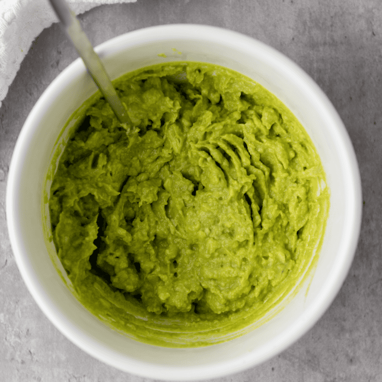 Ripe Hass avocado halves scooped into a glass bowl with fresh lime juice and kosher salt.