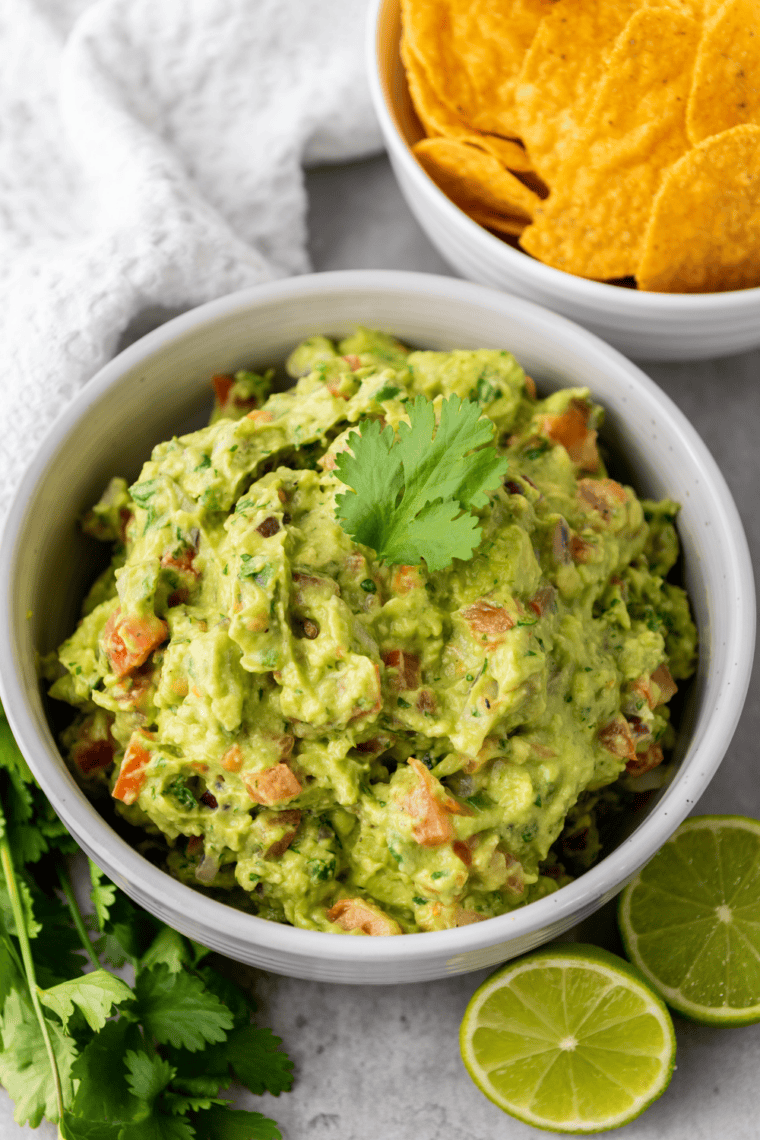 Homemade guacamole Chipotle-style in a rustic bowl with tortilla chips on the side
