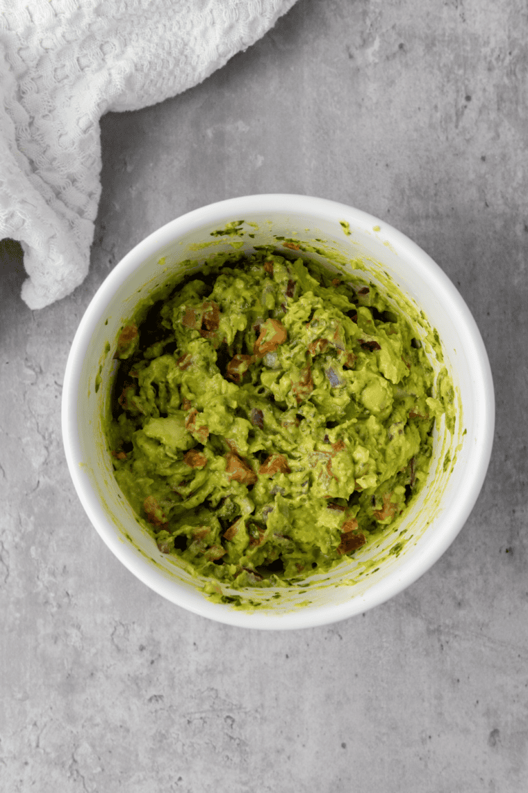 Finished Chipotle guacamole recipe garnished with cilantro and diced tomatoes, ready to serve with tortilla chips