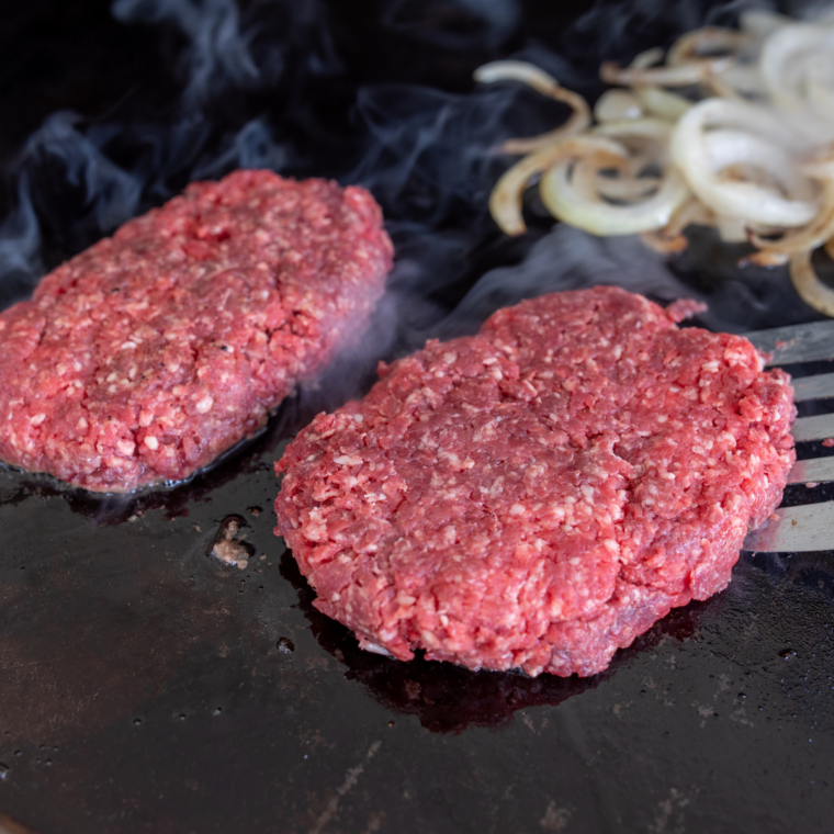 Hot cast iron skillet on stovetop with a thin layer of oil, lightly smoking for smash burger searing.