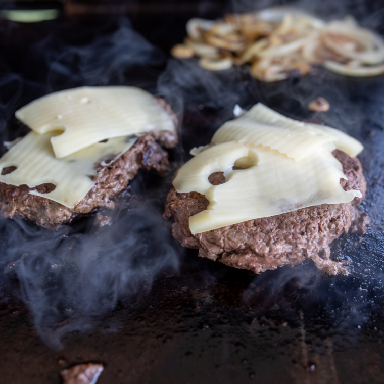 Smash burger patty sizzling in a hot pan, seasoned with salt and pepper while developing a deep crust.