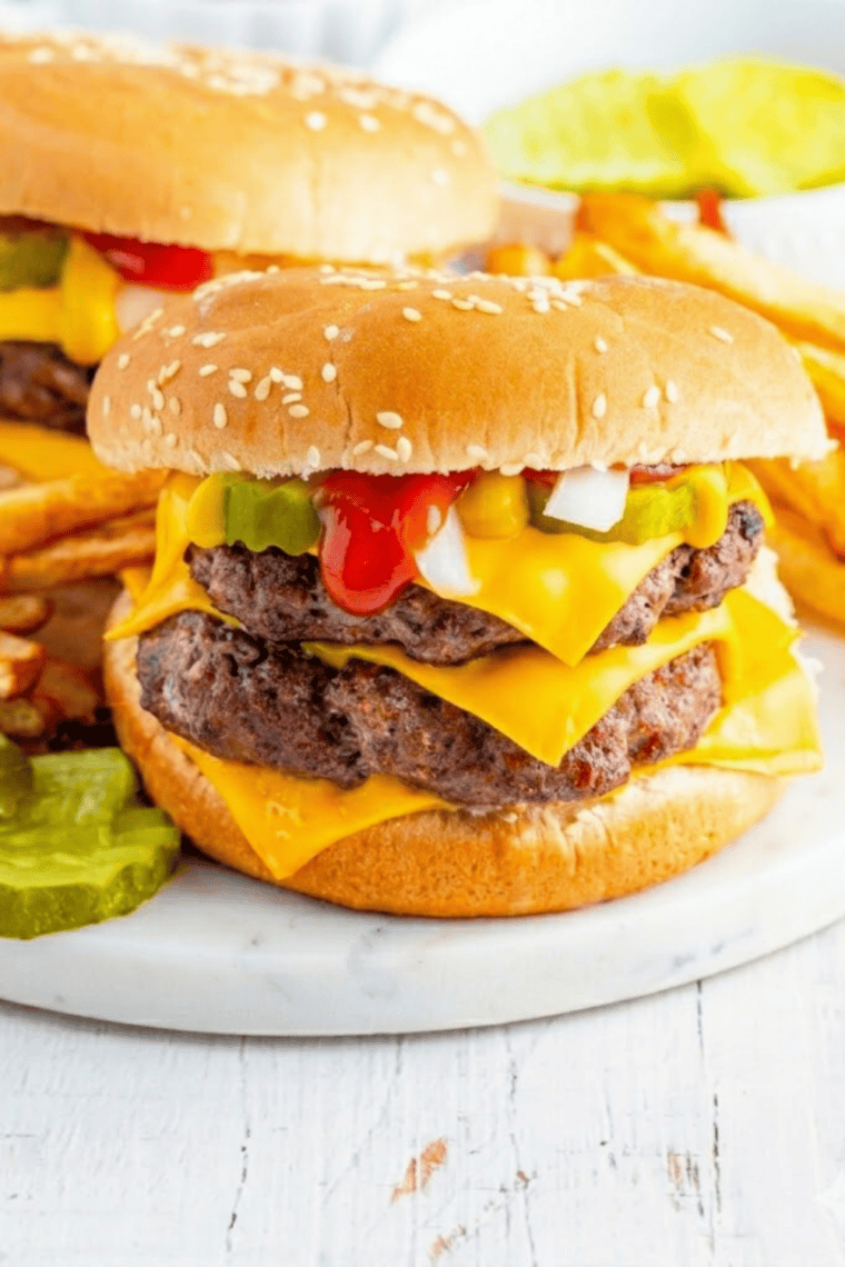 Close-up of double cheeseburger copycat with American cheese, onions, pickles, and beef patties stacked on toasted bun