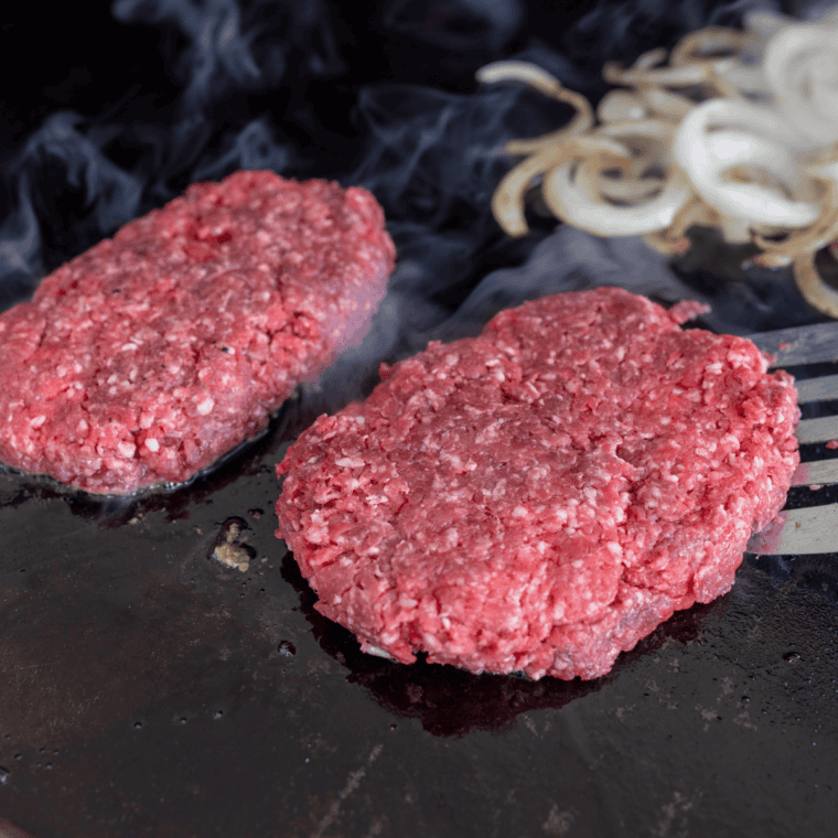 Smash burger patties searing in skillet, flipped with melted American cheese on top