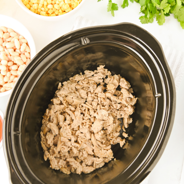 Cooked ground chicken being transferred from a skillet into a crock pot for slow cooker buffalo chicken chili