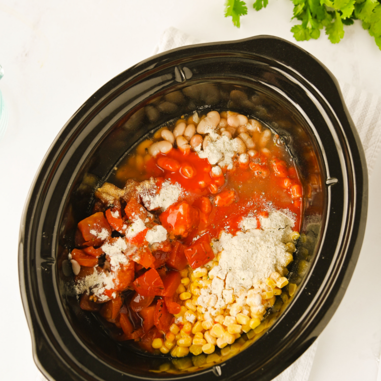 Buffalo wing sauce and chicken broth being poured into a slow cooker filled with chili ingredients