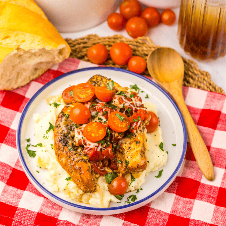Crockpot bruschetta chicken topped with melted mozzarella, fresh cherry tomatoes, and basil on a white plate