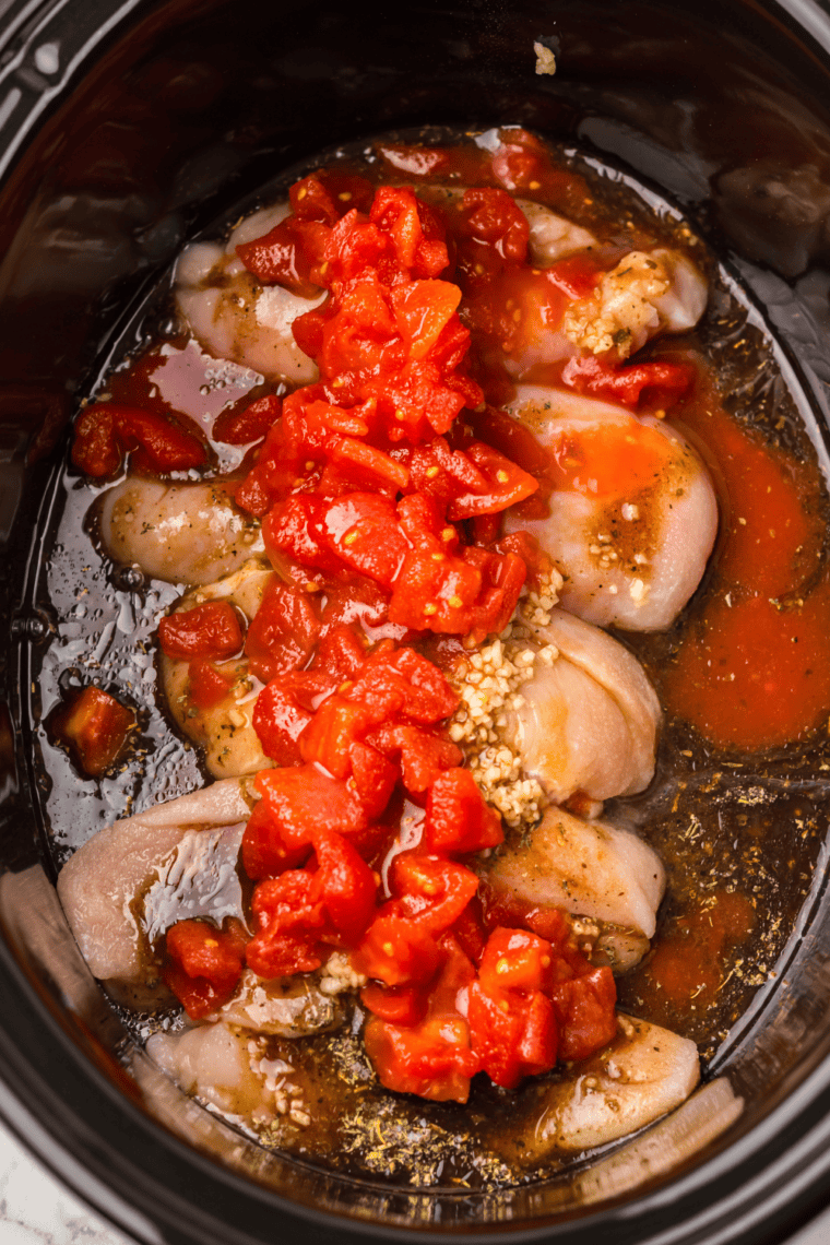 Diced tomatoes and balsamic vinaigrette poured over seasoned chicken breasts in a slow cooker.