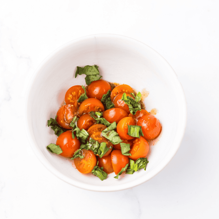 Fresh bruschetta topping with cherry tomatoes and basil in a small white bowl