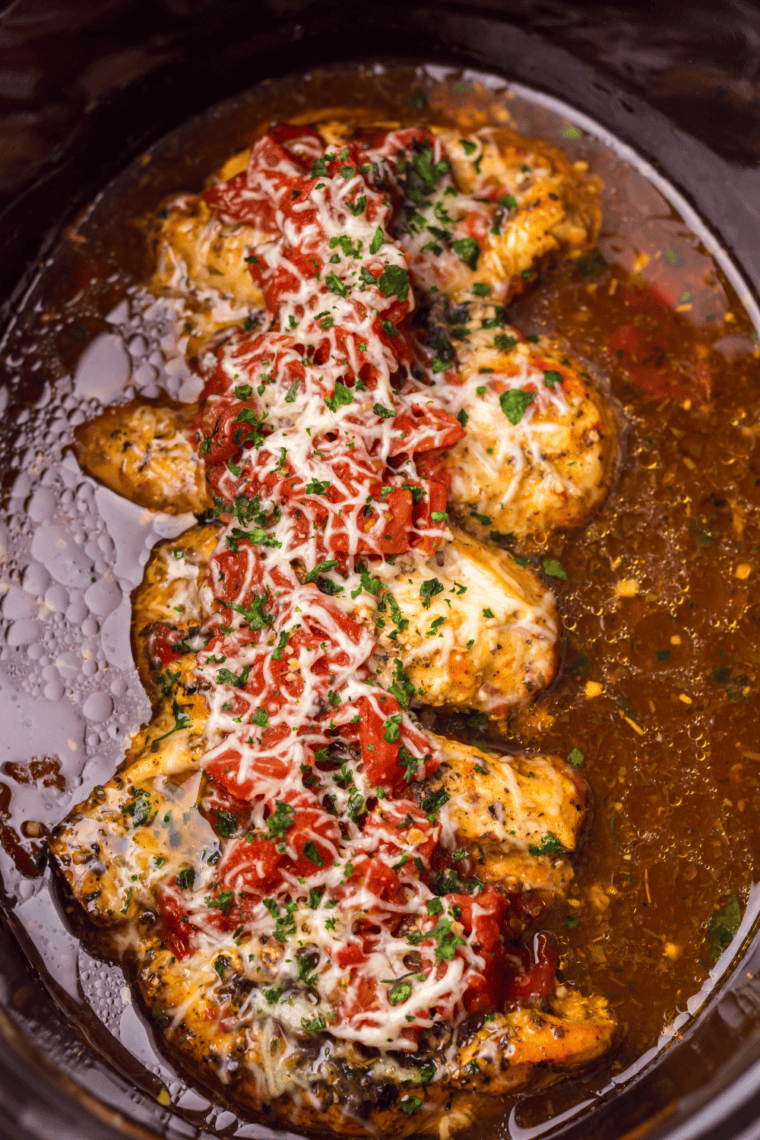 Cooked tender chicken breasts in tomato balsamic sauce inside a slow cooker.
