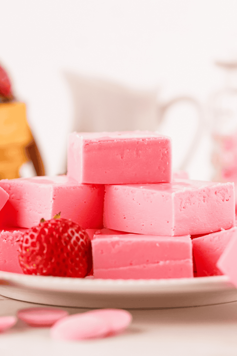 Pink strawberry fudge squares stacked on a plate with a creamy texture and soft edges.
