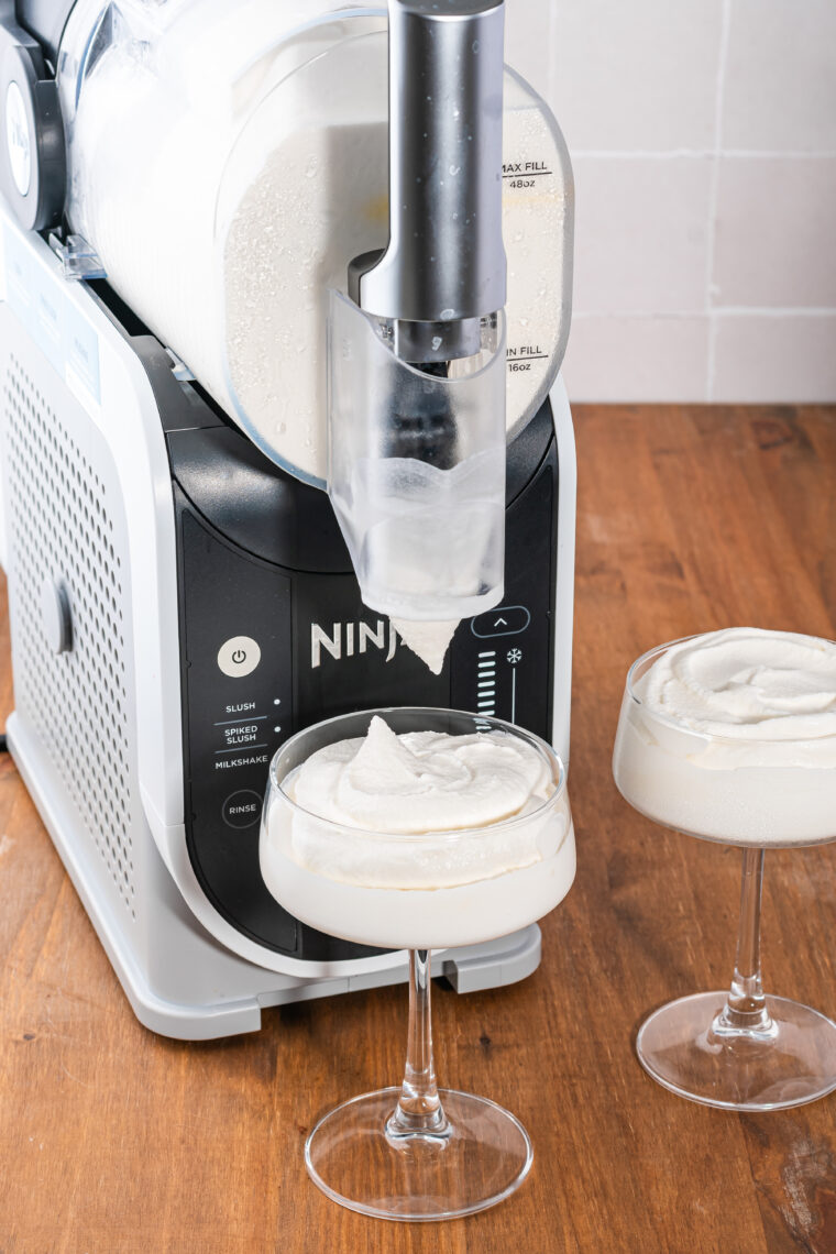 Frozen Brandy Alexander being poured into coupe glass topped with whipped cream and nutmeg garnish