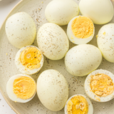 Ninja Crispi hard boiled eggs peeled and sliced on a white plate with seasoning