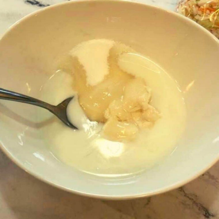 Medium bowl with creamy coleslaw dressing being whisked together using mayonnaise, sugar, vinegar, milk, lemon juice, salt, and pepper until smooth and well blended