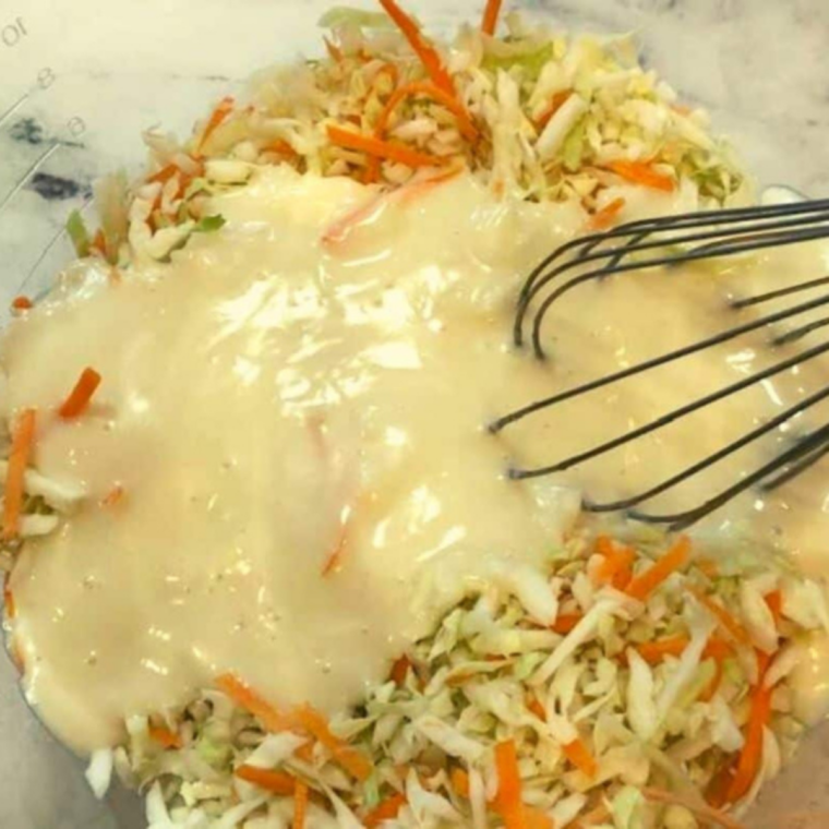 Shredded cabbage and carrots being mixed with creamy dressing in a bowl to make coleslaw, ready to chill and develop flavor in the refrigerator