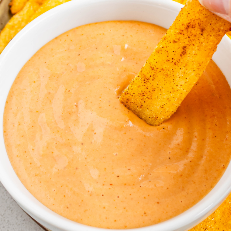 Bowl of creamy orange Popeyes signature sauce served with crispy fried chicken tenders