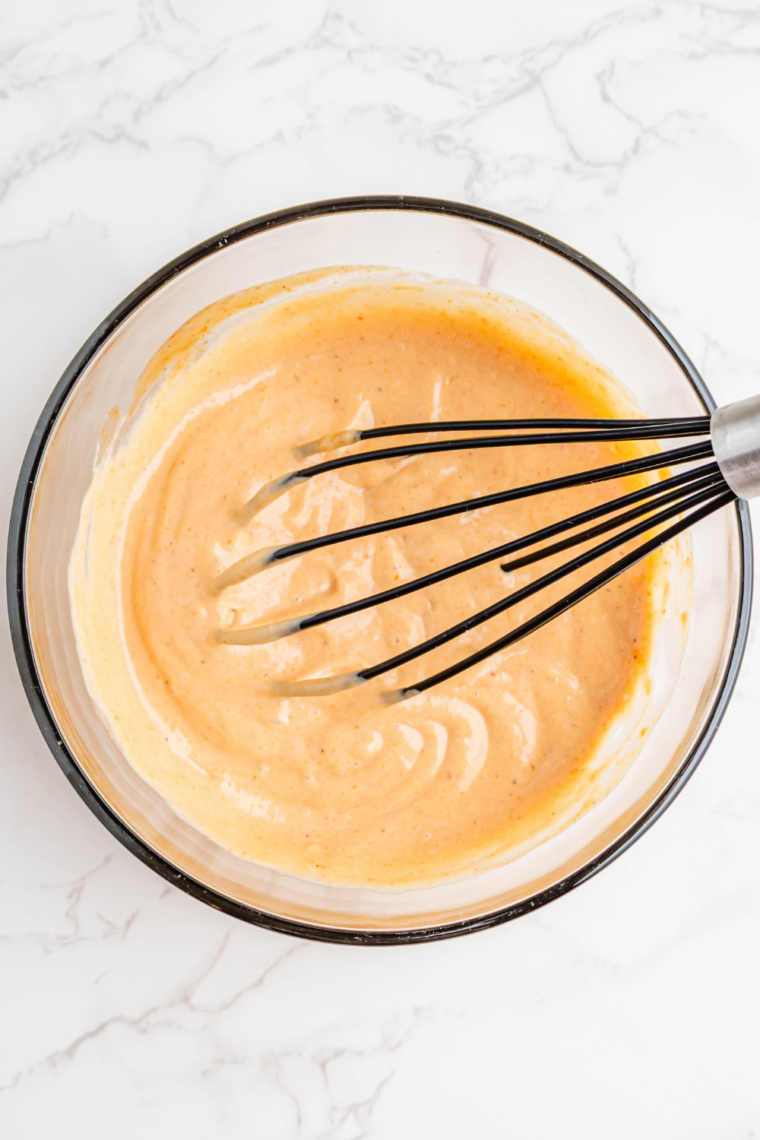 Creamy Popeyes-style sauce being whisked until smooth and glossy in a bowl
