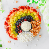 Rainbow fruit tray with marshmallow clouds and Rolo gold arranged on a round serving tray for St. Patrick's Day