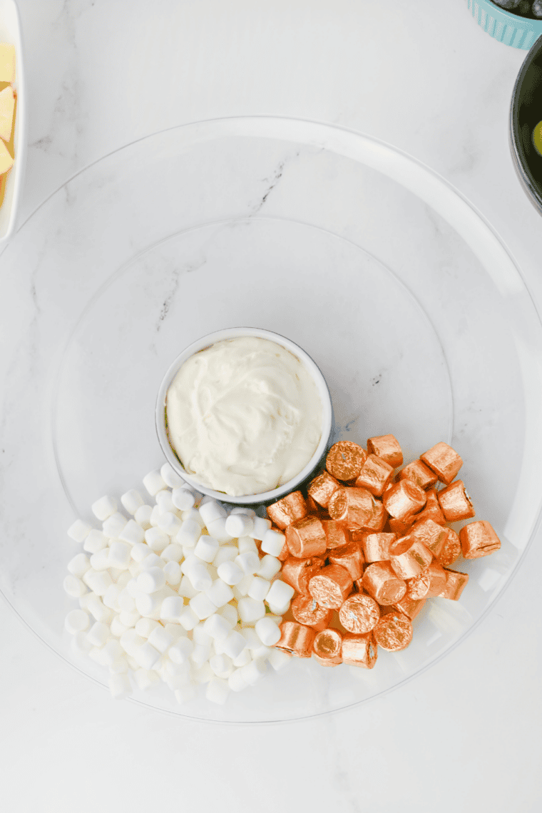 Mini marshmallow clouds and gold Rolo candies forming a pot of gold at the base of a rainbow fruit tray