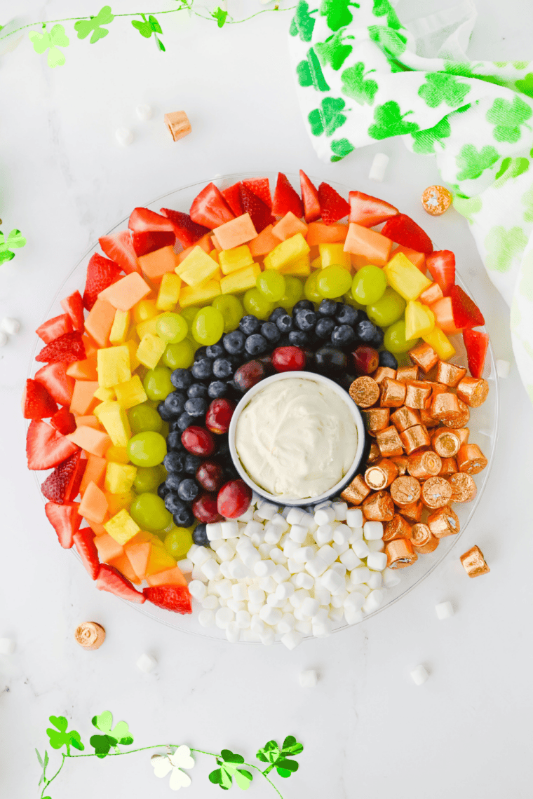 Rainbow fruit board served on a wooden table with a small bowl of fruit dip in the center