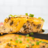 Cheesy venison casserole in a cast iron skillet with melted cheddar bubbling on top