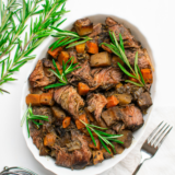 Homemade pot roast seasoning blend in a small bowl with dried herbs and spices on a wooden table.
