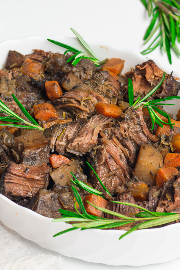 Homemade pot roast seasoning blend in a glass jar with dried herbs and spices on a wooden countertop.