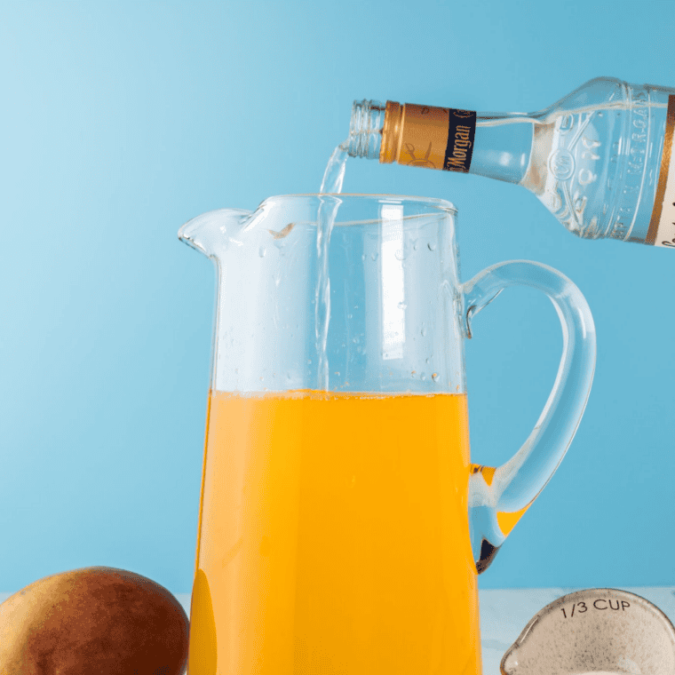 Ninja Slushi vessel filled with mango nectar, tequila, triple sec, lime juice, simple syrup, and water being stirred before blending mango margarita mixture