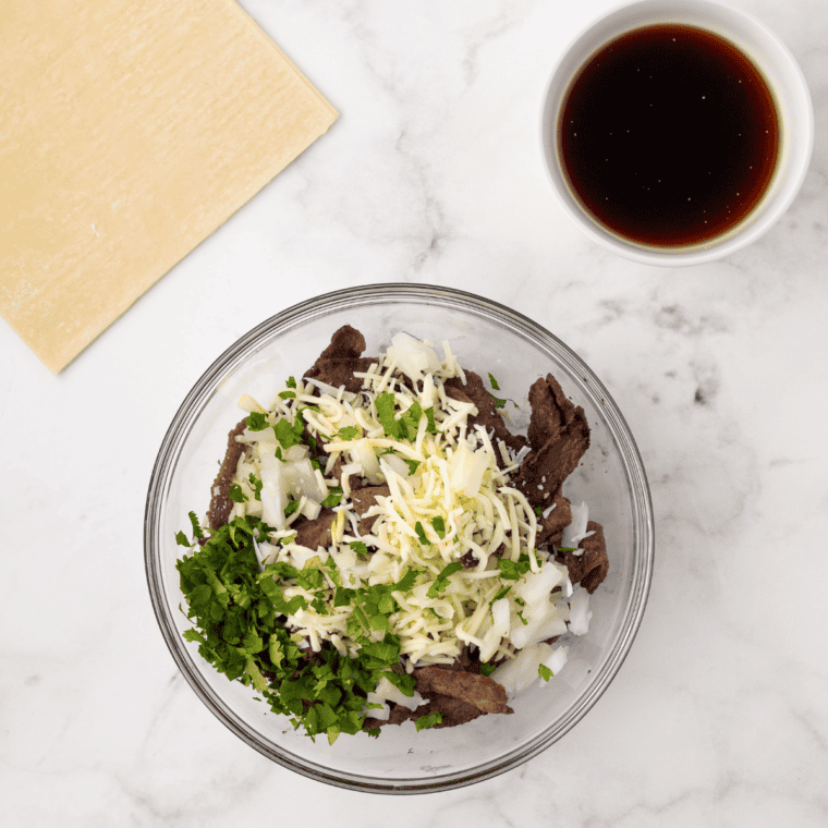 Shredded birria beef draining in a strainer over reserved consomm&eacute;