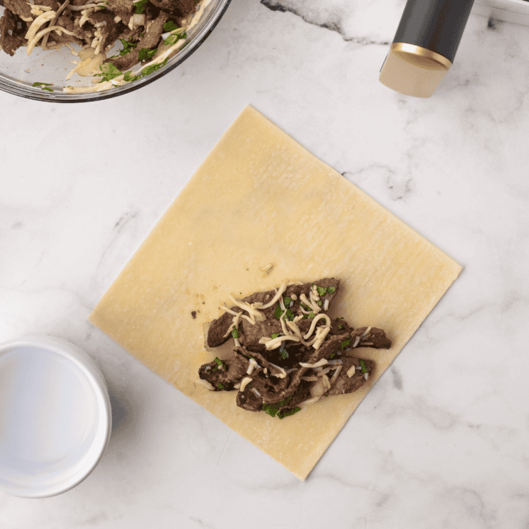 Shredded birria beef and cheese rolled into an egg roll wrapper on a diamond-shaped wrapper