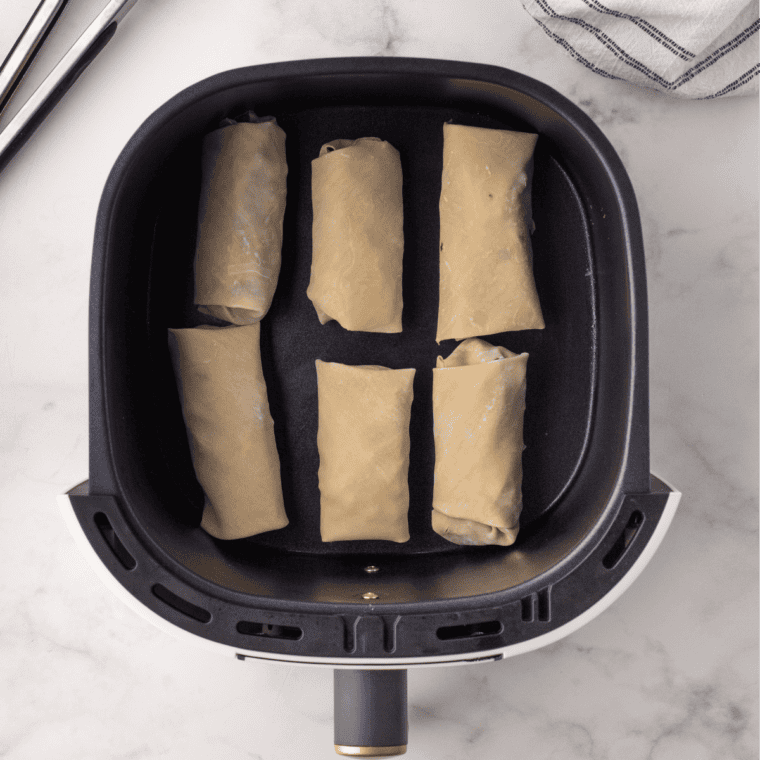 Birria egg rolls arranged seam-side down in an air fryer basket