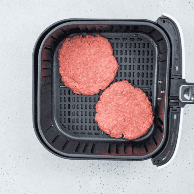 Beef balls smashed flat into thin patties on a parchment round in the air fryer basket