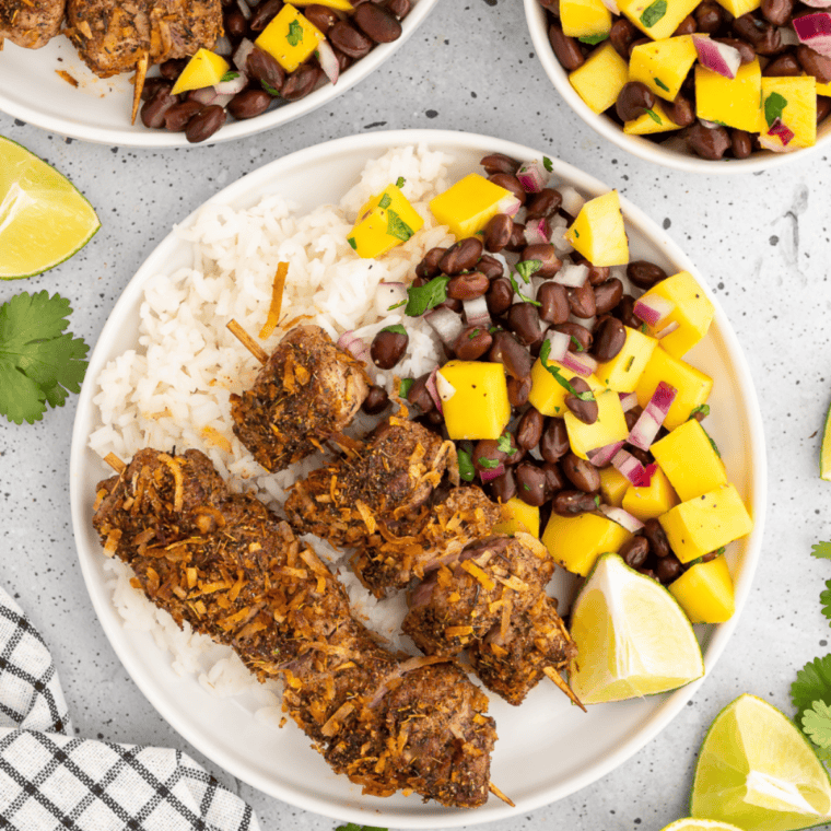Jerk pork tenderloin skewers on a plate with fresh mango black bean salsa.