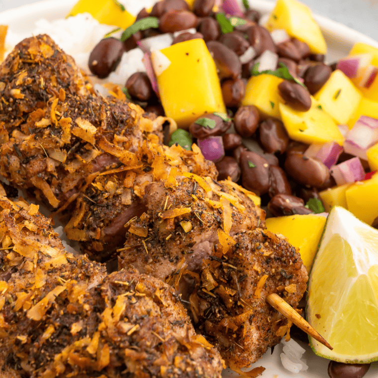 Close up of air fryer jerk pork skewers served on a plate with fresh black bean mango salsa, featuring juicy seasoned pork, sweet mango, black beans, and colorful vegetables in a quick 30 minute meal.