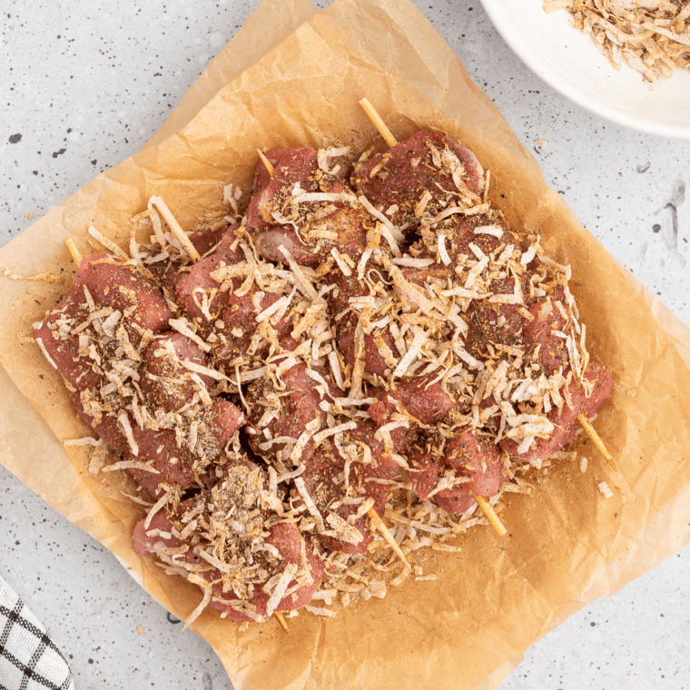 Sprinkling coconut-jerk seasoning mixture over pork skewers.