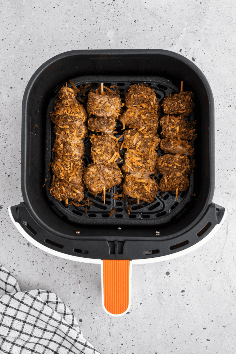 Jerk pork skewers cooking in a single layer in the air fryer basket.