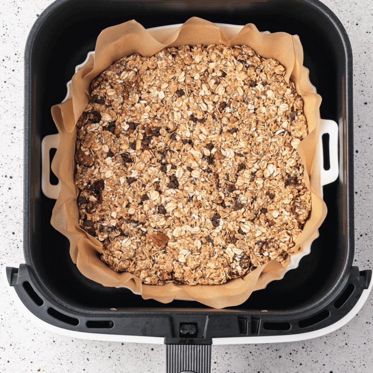 Air fryer peanut butter granola spread on parchment in the basket.