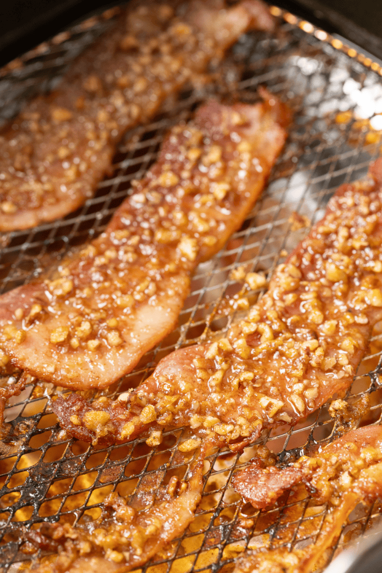 Air fryer praline bacon strips coated in caramelized brown sugar and toasted pecans on parchment paper
